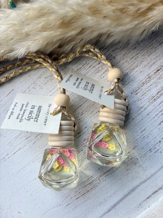 Two small glass bottles with floral decorations on a textured surface with tags.