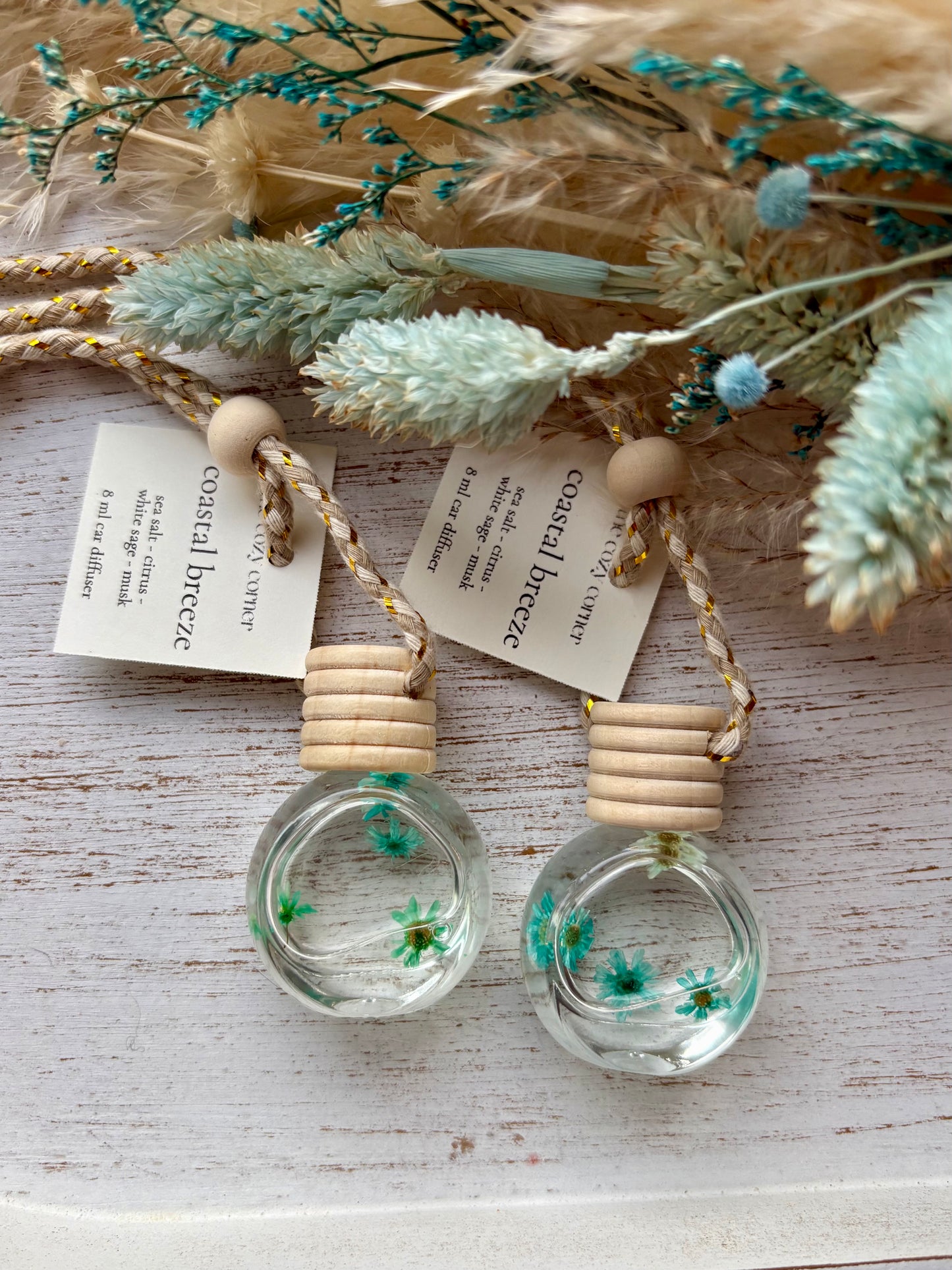 Two small glass bottles with wooden tops, containing dried flowers, on a rustic wooden surface.
