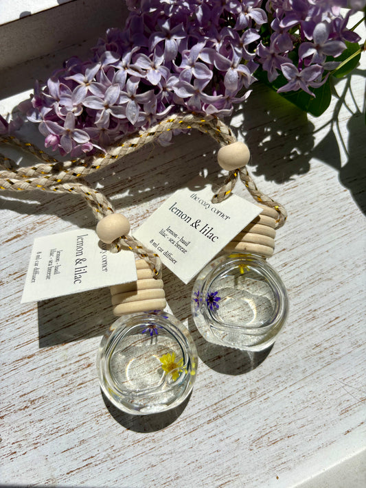 Two small glass containers with floral elements on a wooden surface with purple flowers in the background.