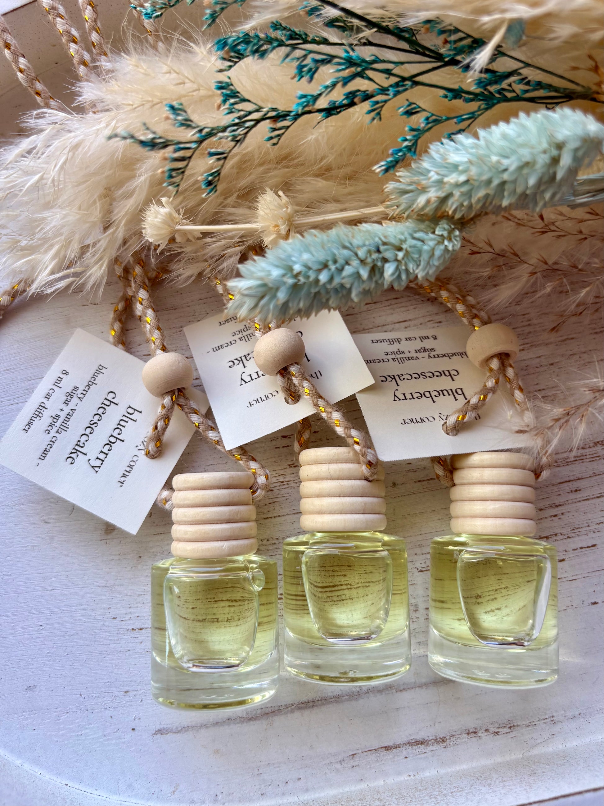 Three small glass bottles with wooden caps on a white surface with decorative elements.