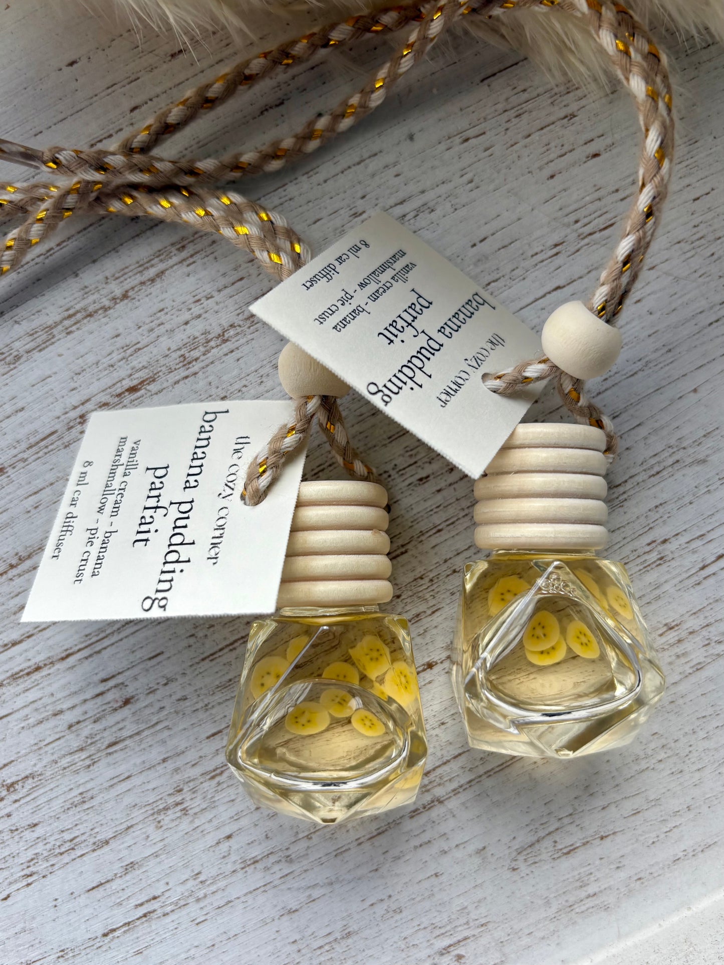 Two small glass bottles with wooden tops on a textured surface, each with a label.