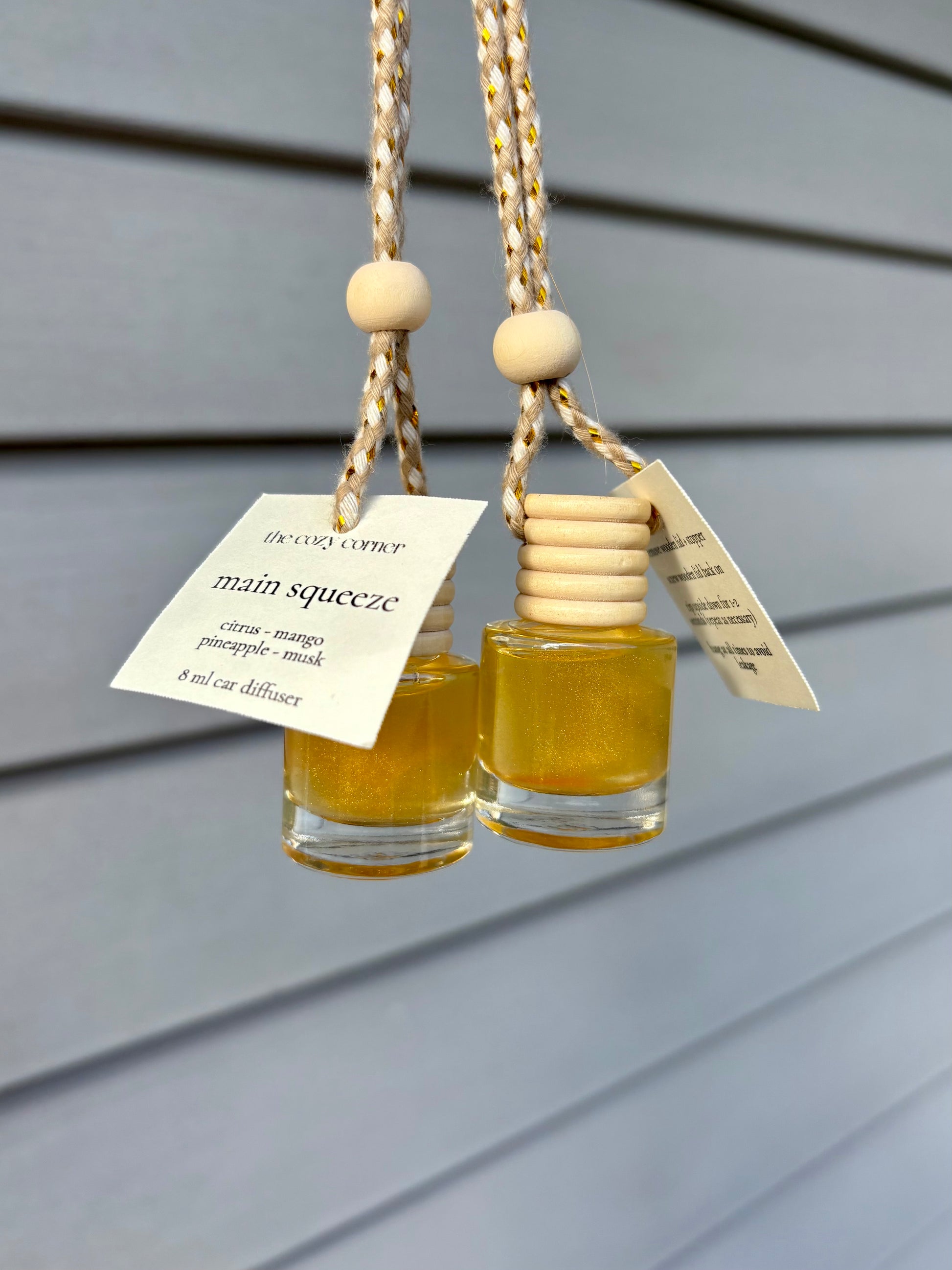 Two small glass bottles with wooden caps hanging against a gray wooden panel background.