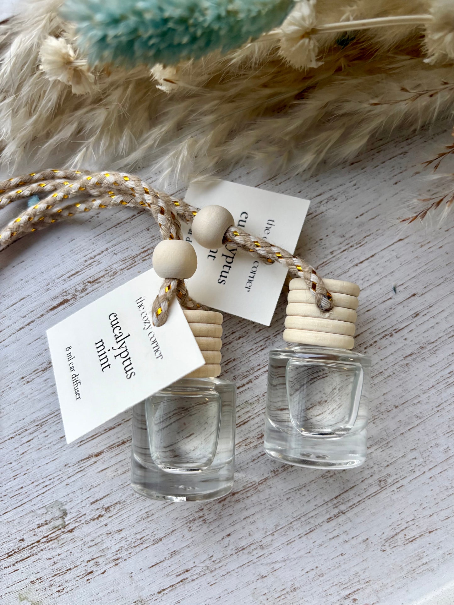 Two small clear bottles with wooden caps on a textured surface with feathers and tags.