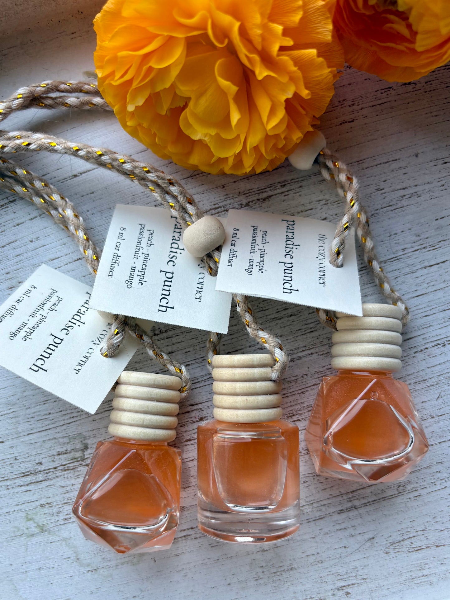 Three small perfume bottles with wooden caps on a textured surface with yellow flowers in the background.