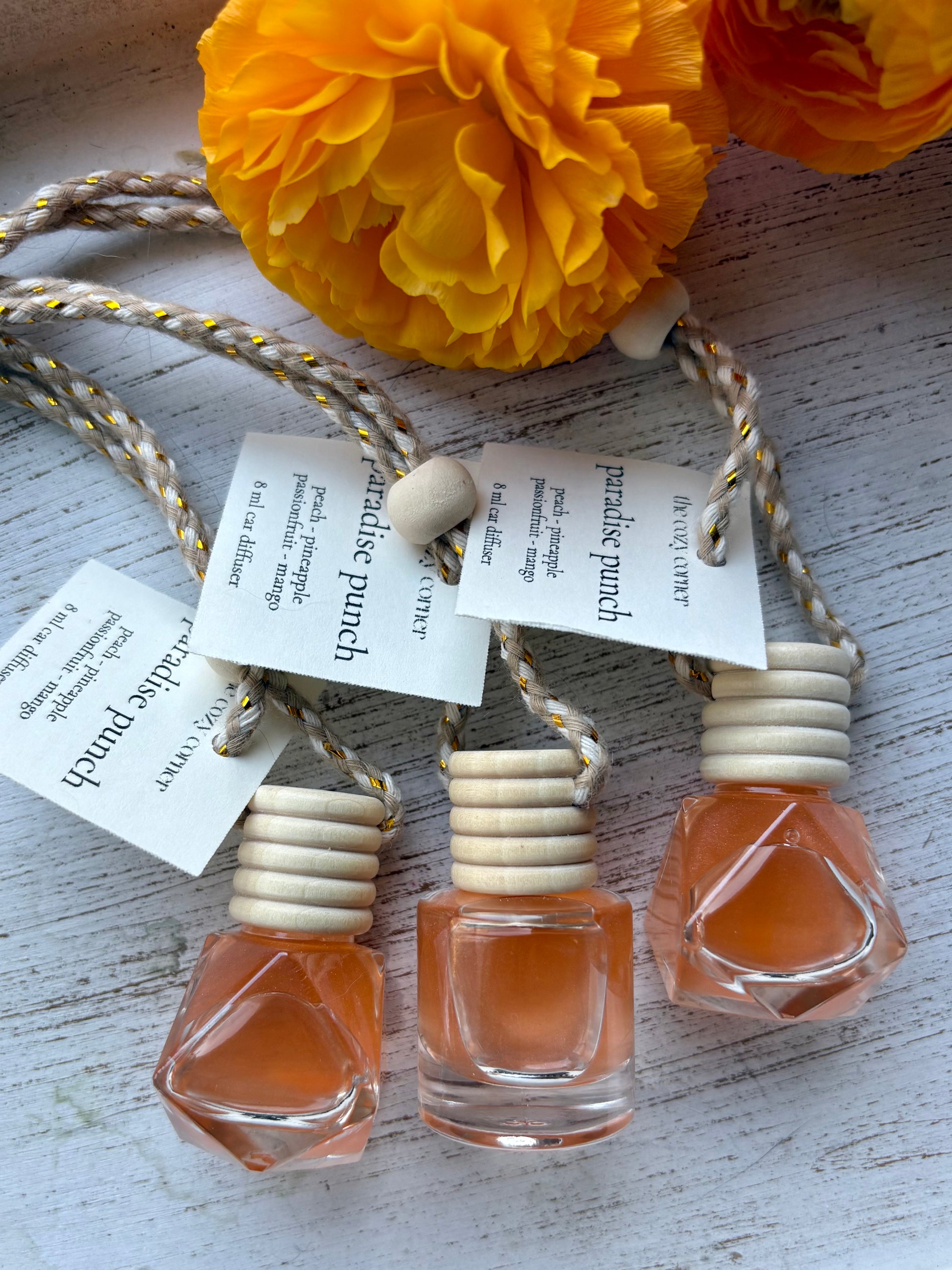 Three small perfume bottles with wooden caps on a textured surface with yellow flowers in the background.