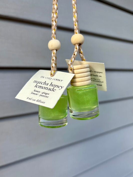Two small glass diffusers with 'matcha honey lemonade' scent hanging against a wooden background.