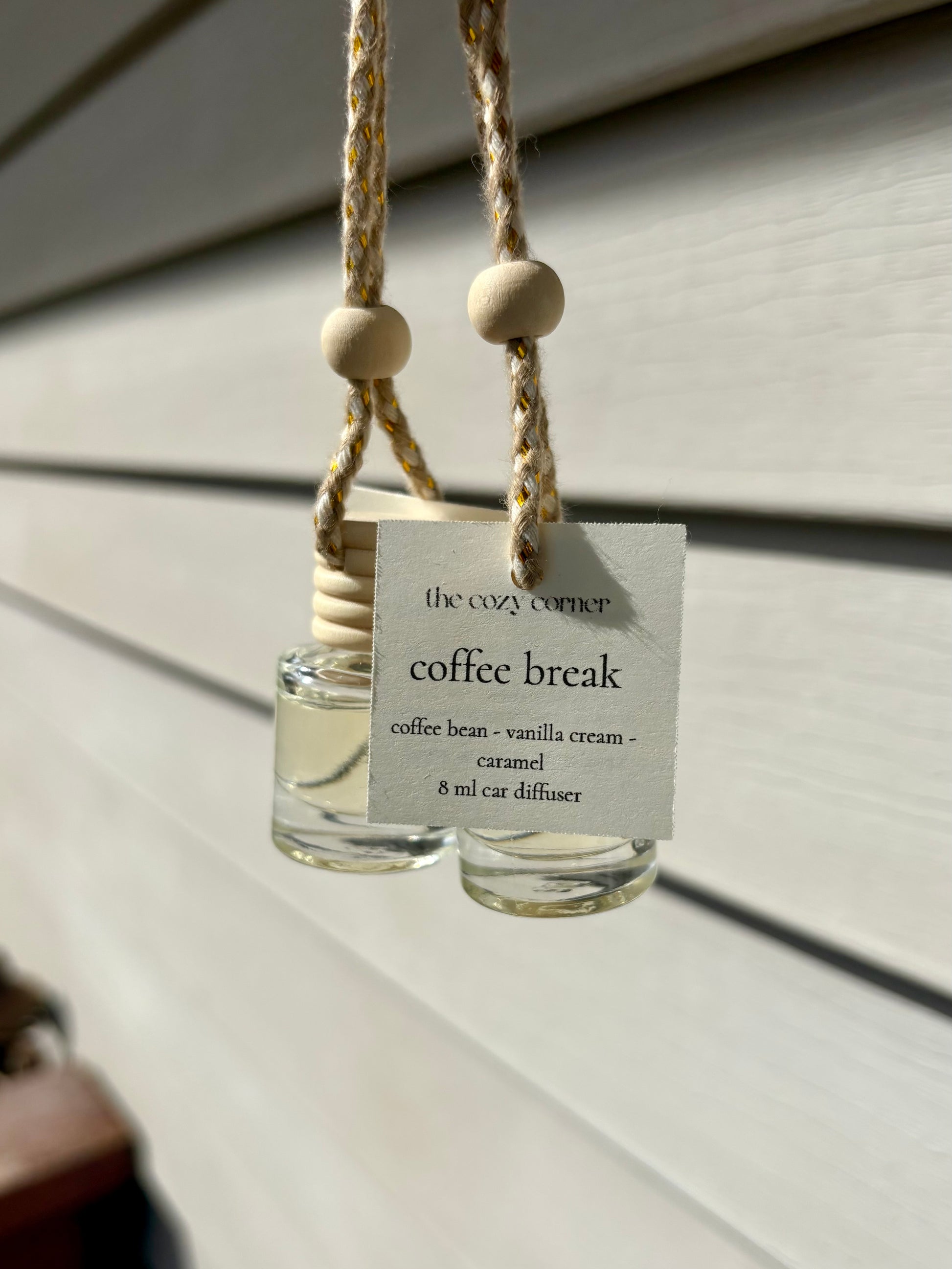 Glass car diffuser labeled 'coffee break' hanging against a neutral background