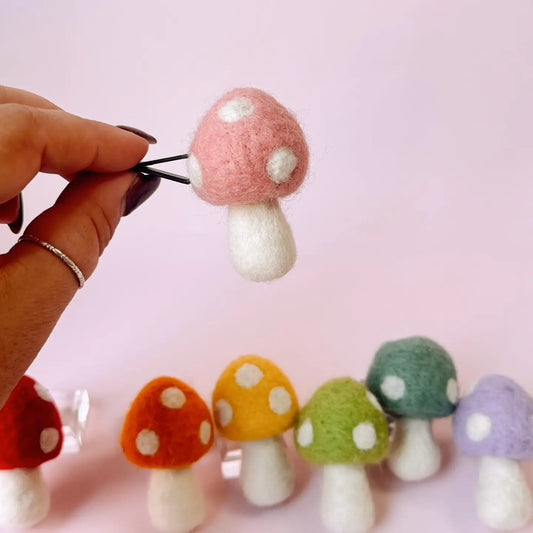 Colorful felt mushroom earrings on a pink background