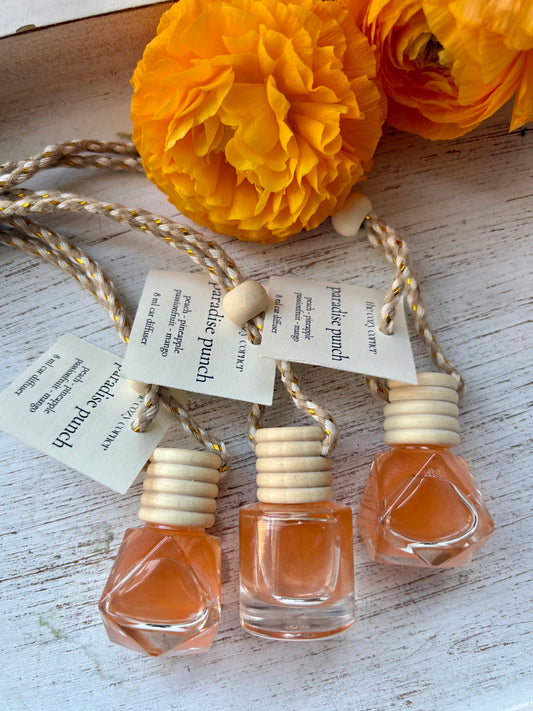 Three small perfume bottles with wooden caps on a string, surrounded by yellow flowers on a rustic wooden surface.
