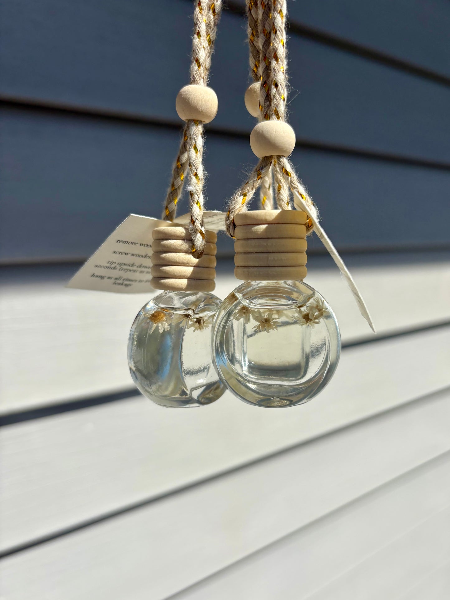 Two hanging glass diffusers with natural elements on a wooden surface
