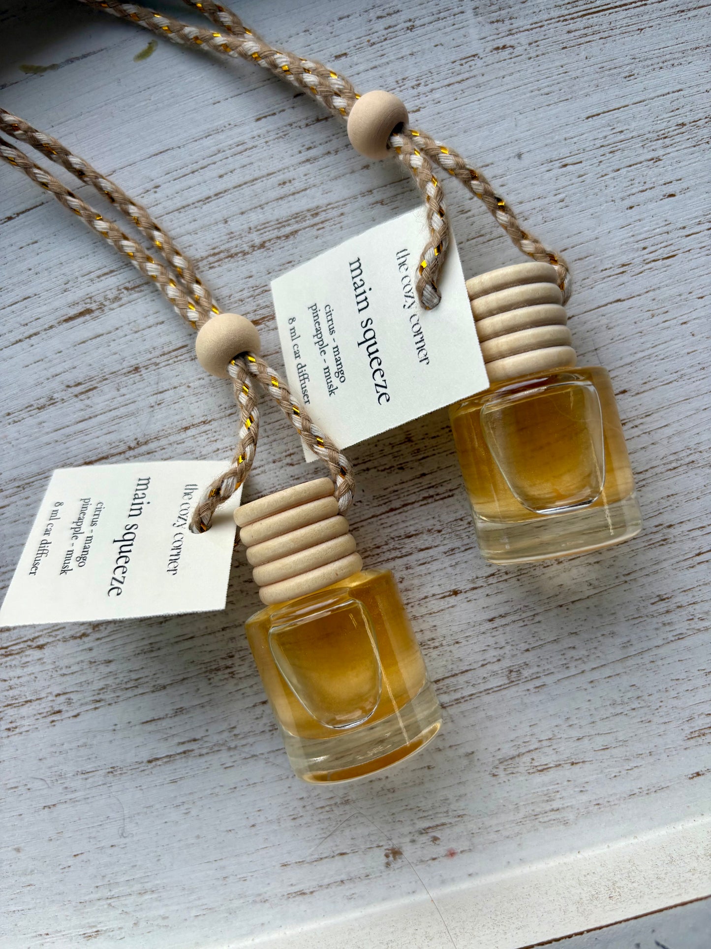 Two small glass bottles with wooden caps hanging from a string on a light wooden surface.