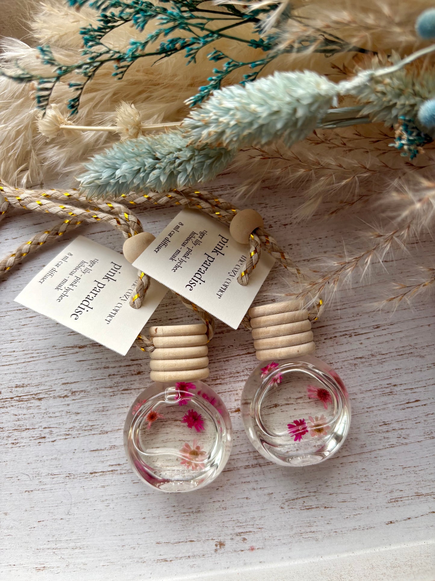 Two small glass bottles with wooden caps on a textured surface with dried plants.