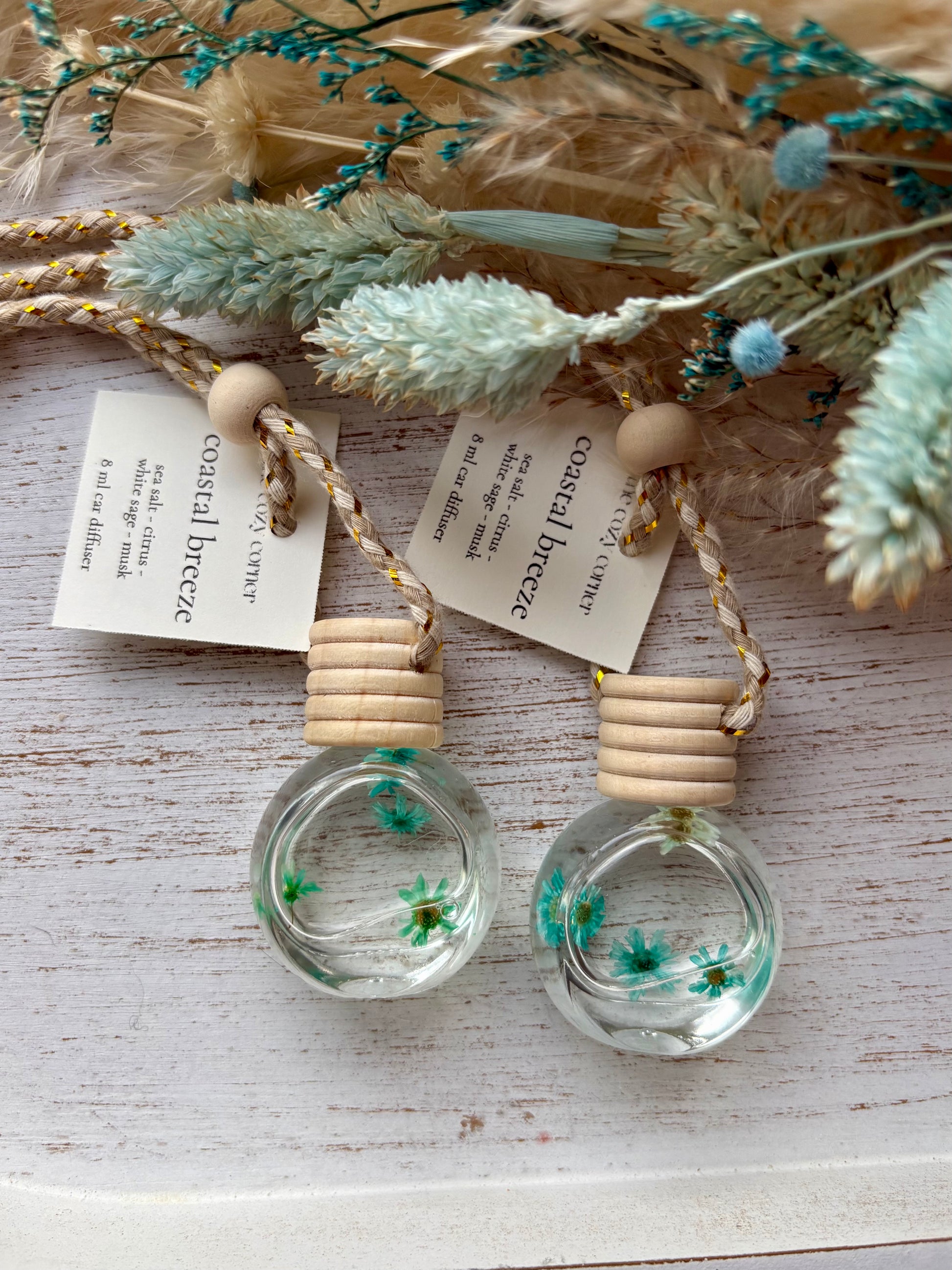 Two small glass bottles with wooden tops, containing dried flowers, on a rustic wooden surface.