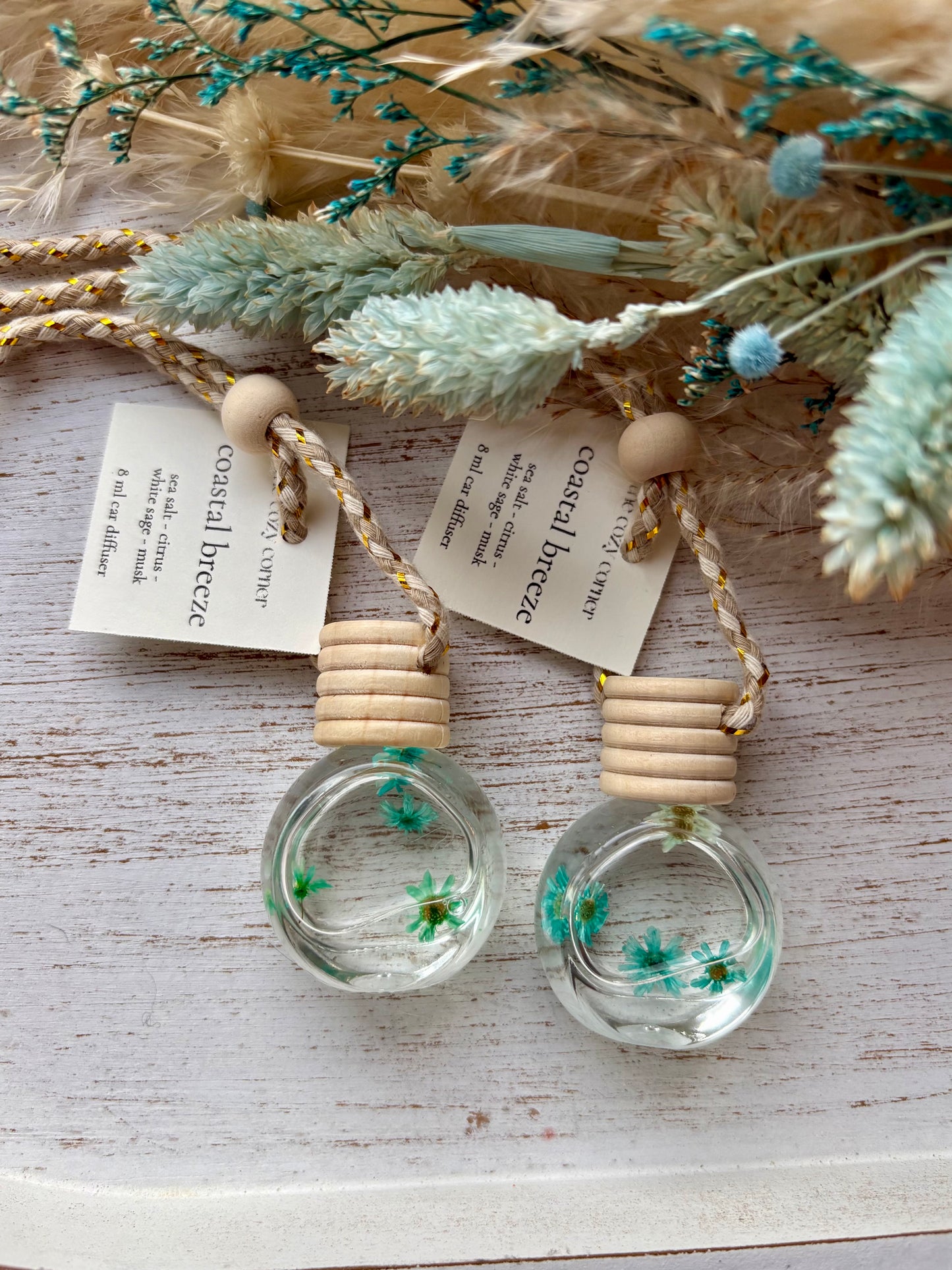 Two small glass bottles with wooden tops, containing dried flowers, on a light wooden surface.