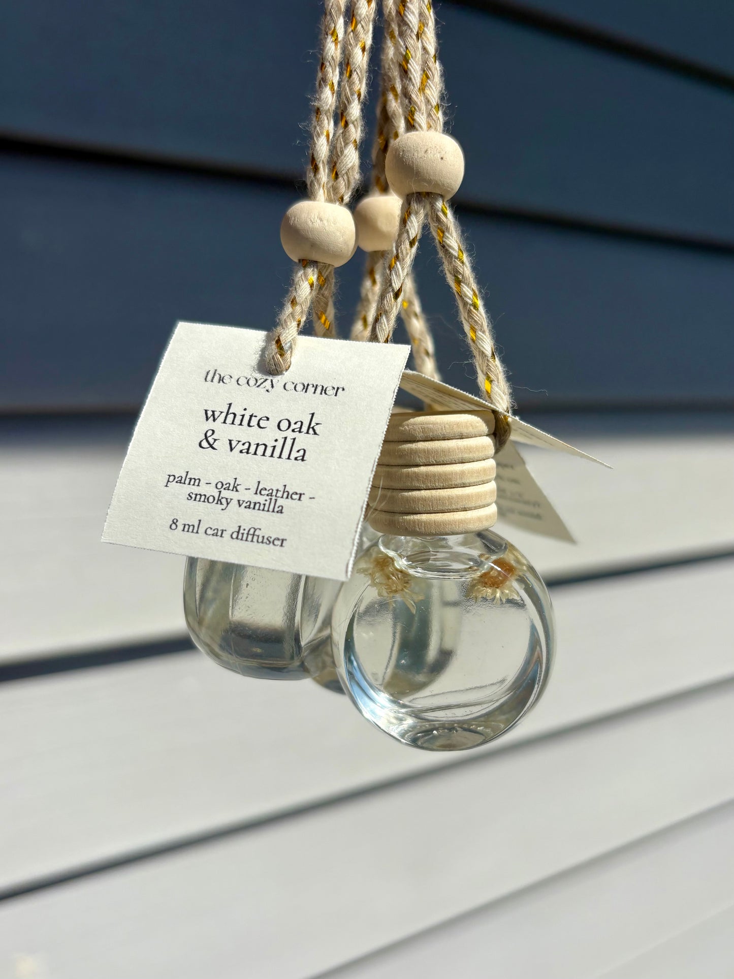 Clear glass car diffuser with wooden beads and a label on a gray surface.