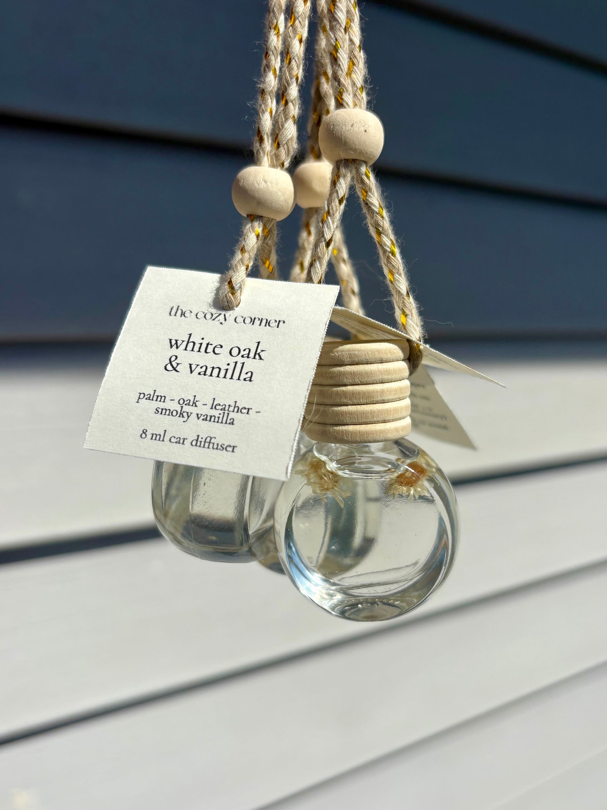 Clear glass car diffuser with wooden beads and a label on a gray surface.