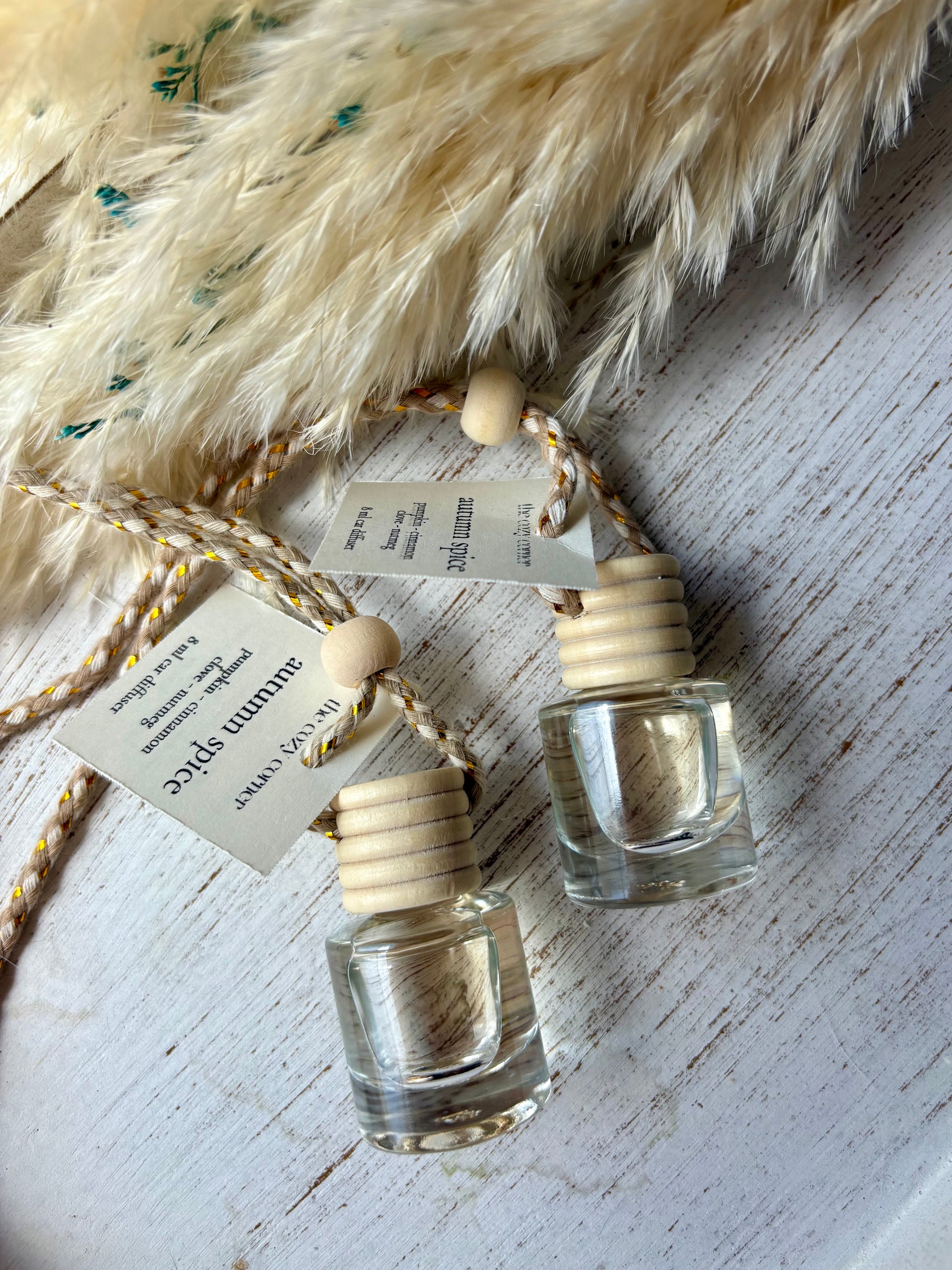 Two small glass bottles with wooden caps on a textured surface with feathers.