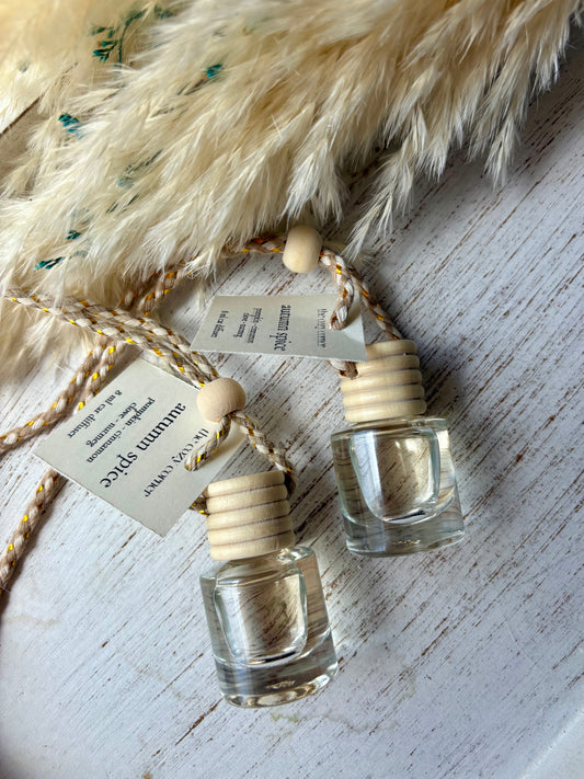 Two small glass bottles with wooden caps on a textured surface with feathers.