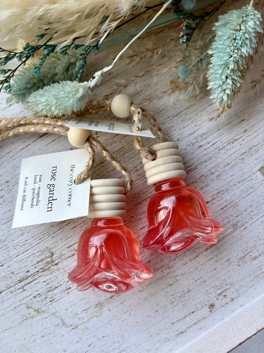 Two small glass bottles shaped like flowers with wooden caps on a rustic surface with dried plants.