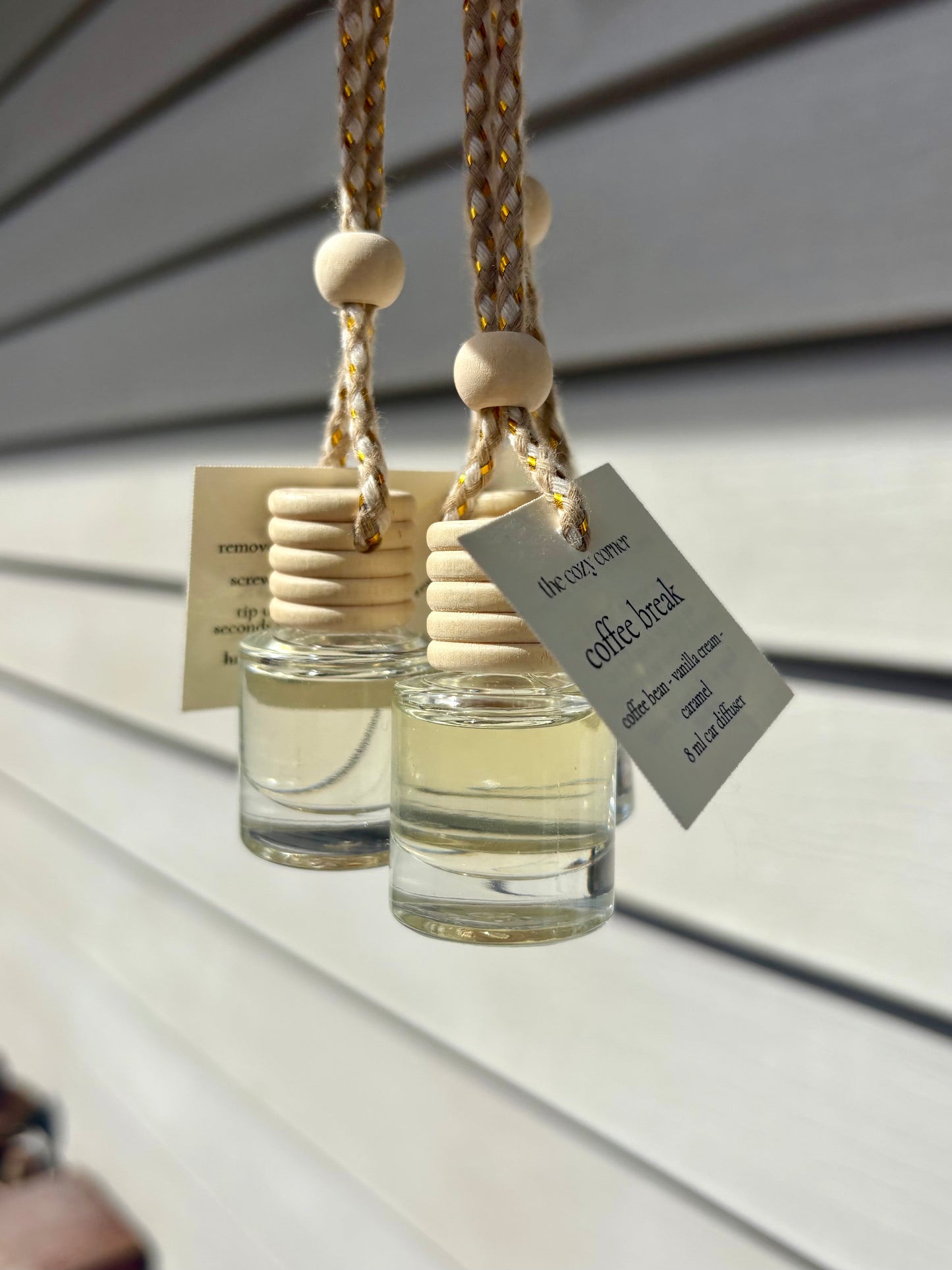 Two small glass bottles with wooden stoppers hanging against a neutral background