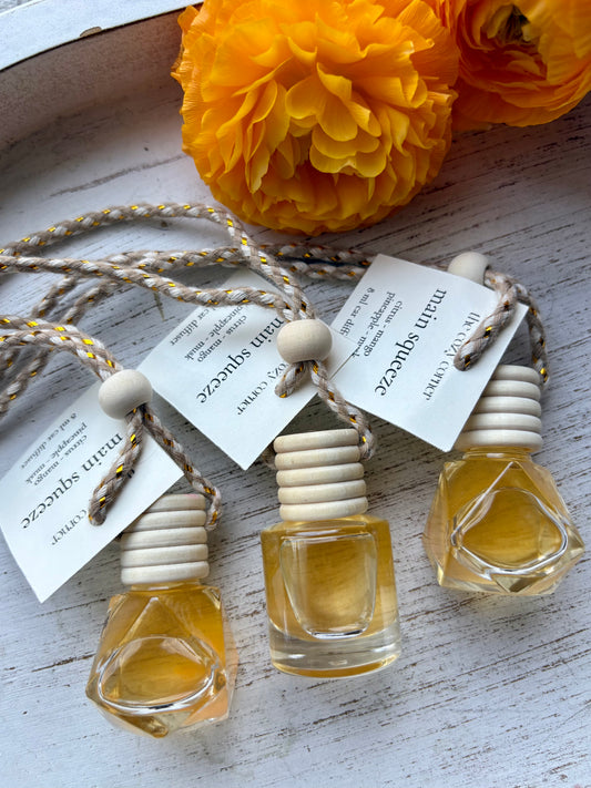 Three small perfume bottles with wooden caps on a white surface with yellow flowers in the background.