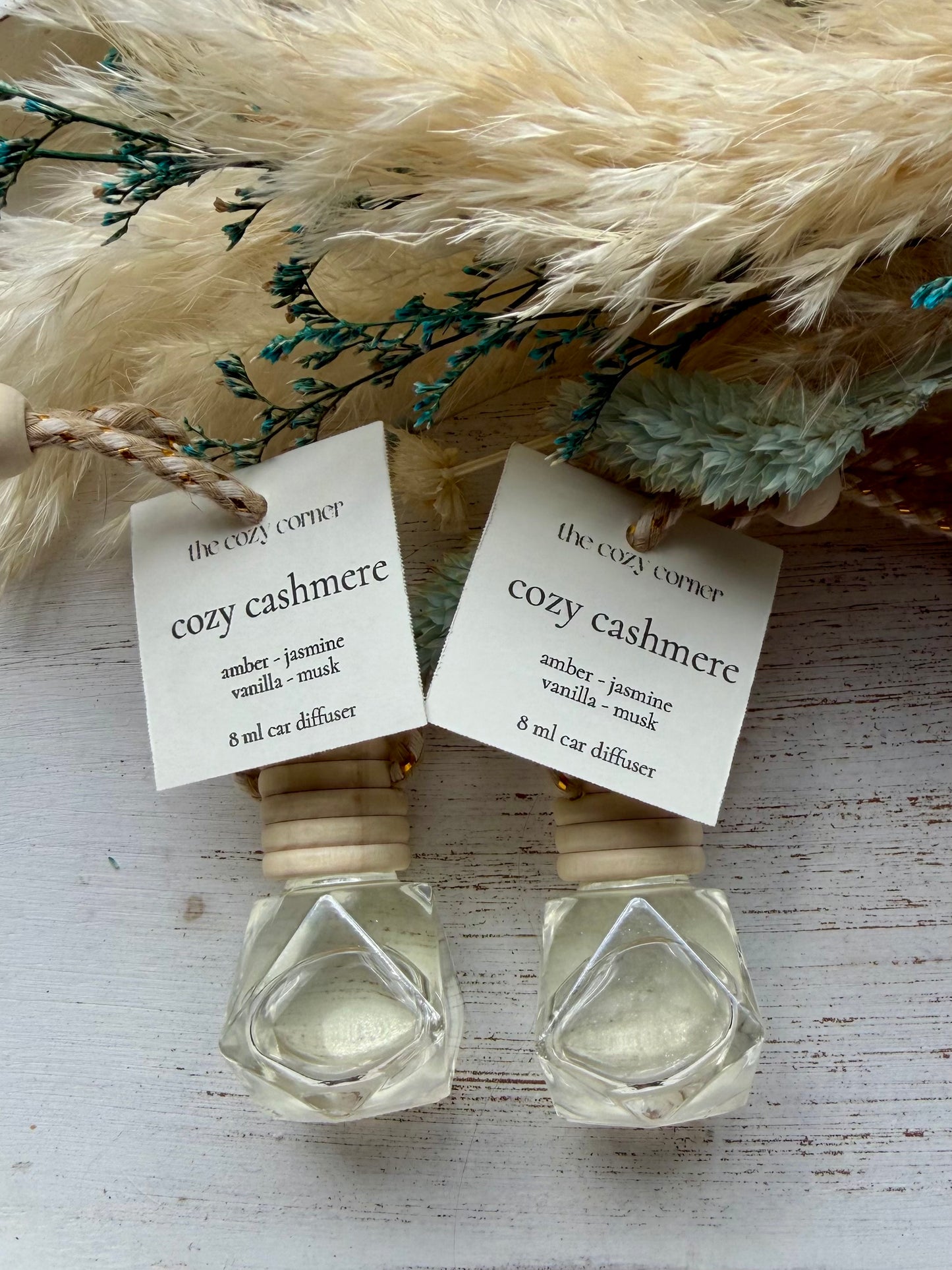 Two 'cozy cashmere' diffusers with labels on a wooden surface with decorative elements.