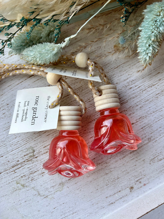 Two small red flower-shaped bottles with wooden caps on a rustic wooden surface with dried plants.