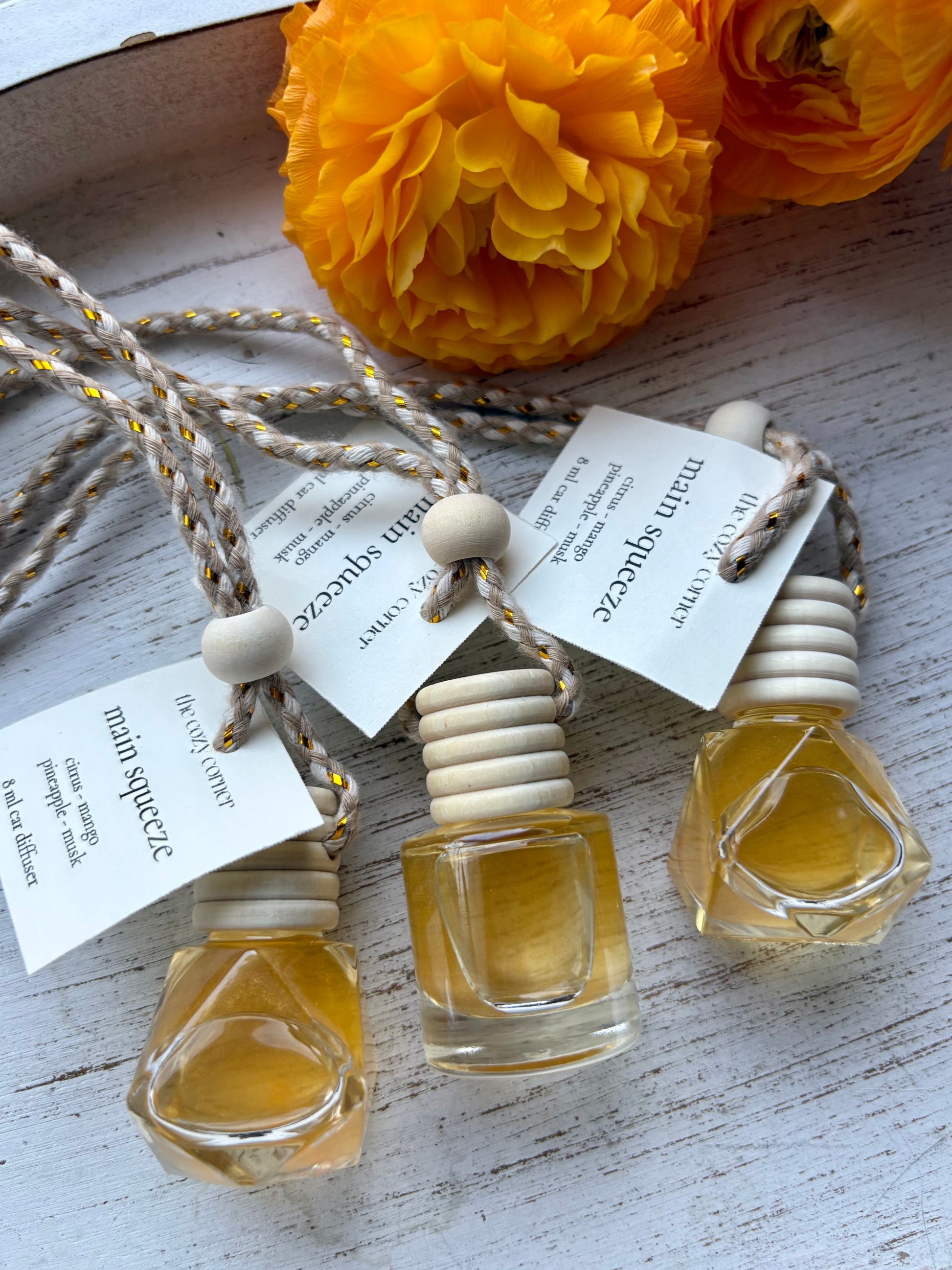 Three small glass bottles with cork stoppers and string labels on a wooden surface with yellow flowers.