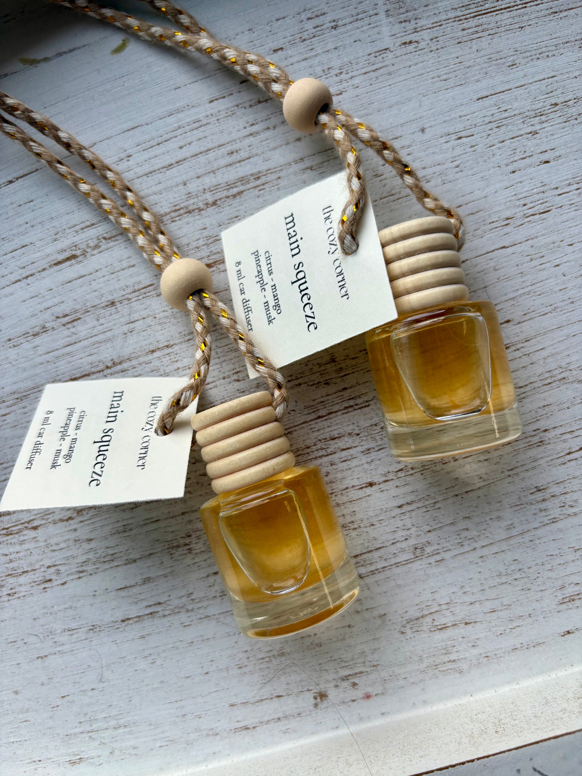 Two small glass bottles with cork stoppers hanging on a string against a light wooden background.