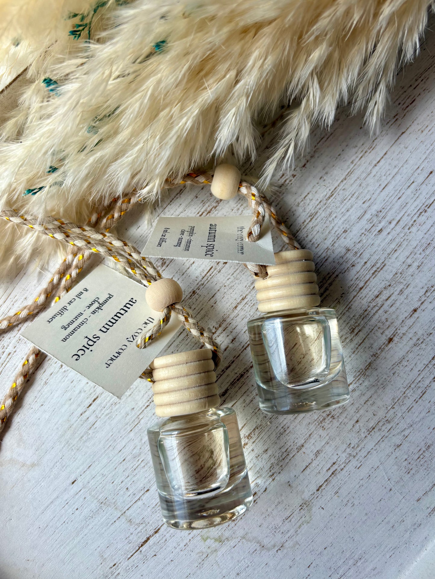 Two small glass bottles with wooden caps on a textured surface with feathers.