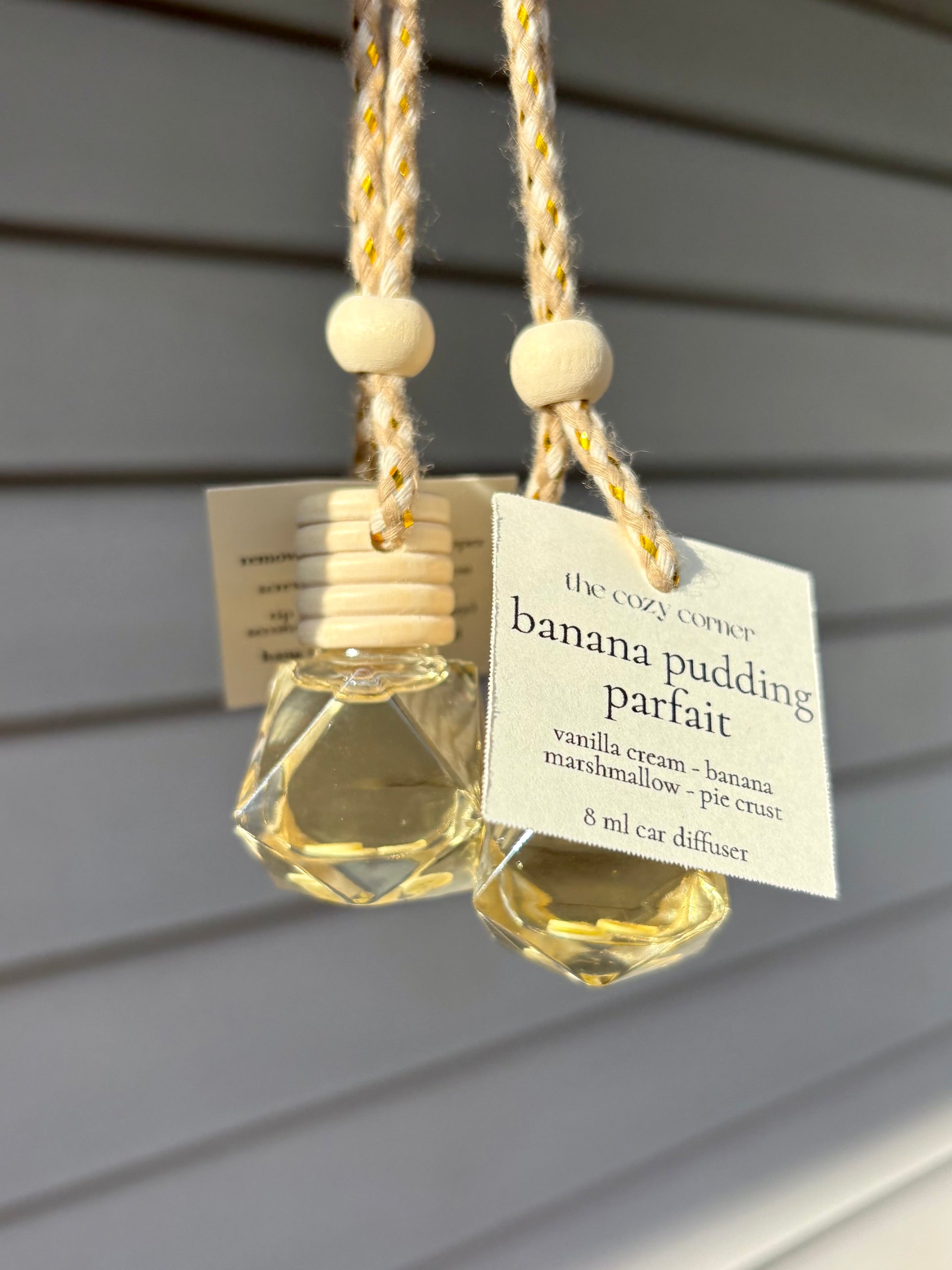 Two hanging car diffusers labeled 'banana pudding parfait' on a neutral background