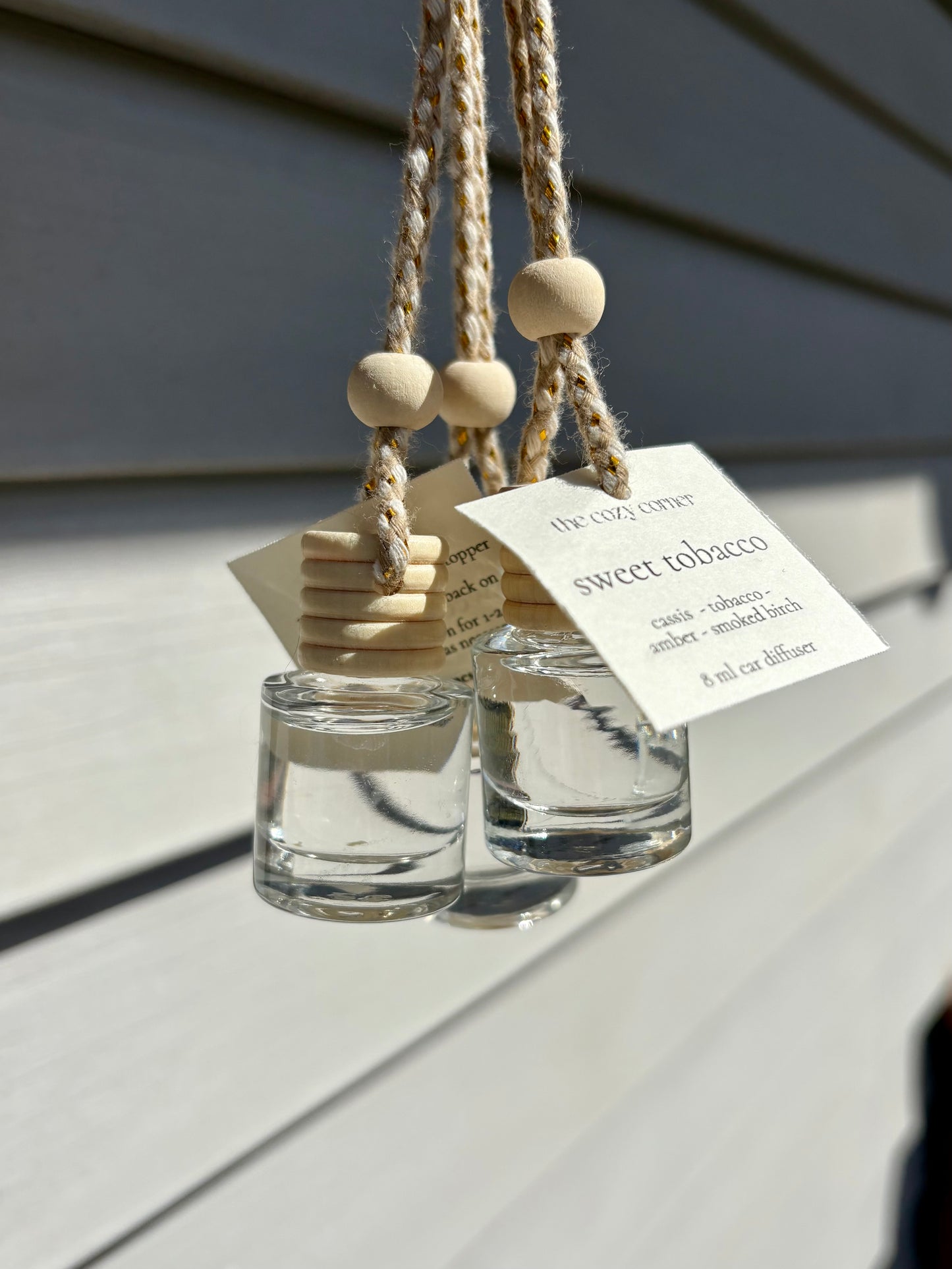 Two glass diffusers with wooden beads hanging on a rope against a gray background.