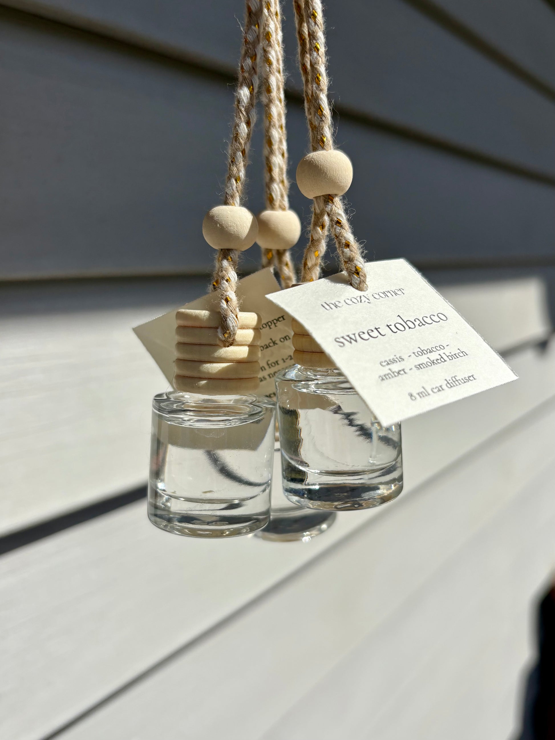 Two glass diffusers with wooden beads hanging on a rope against a gray background.