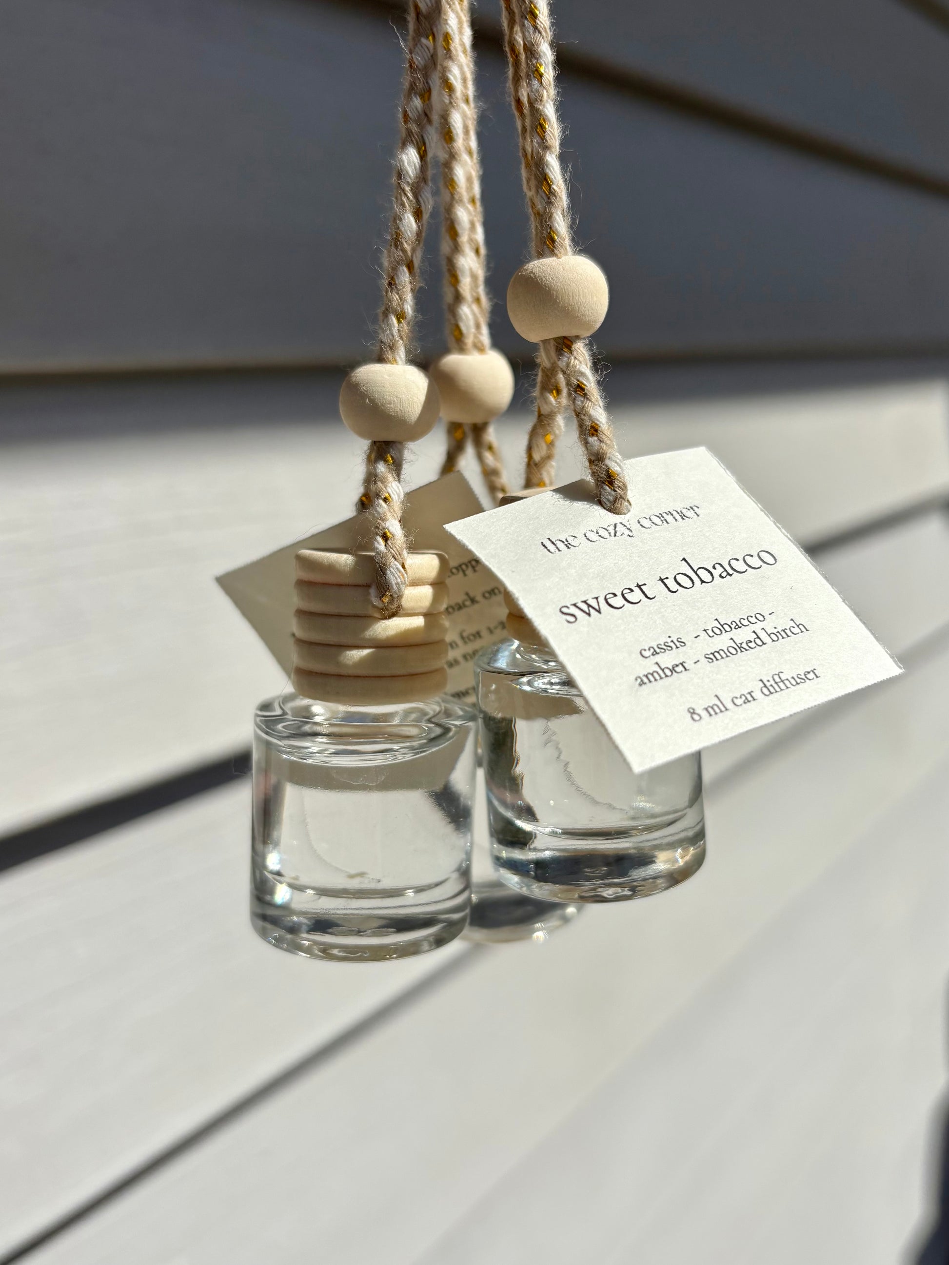 Two small glass diffusers with wooden beads and labels on a light wooden surface.