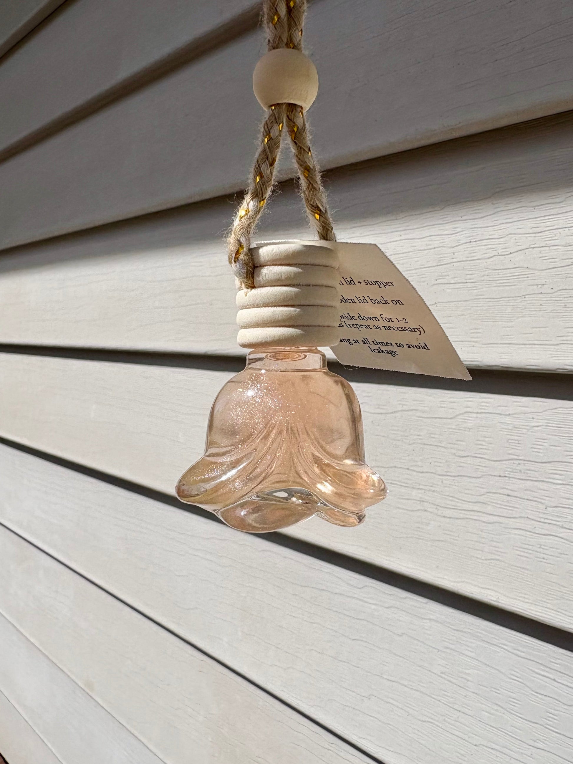 Decorative glass bell hanging on a rope against a wooden wall.