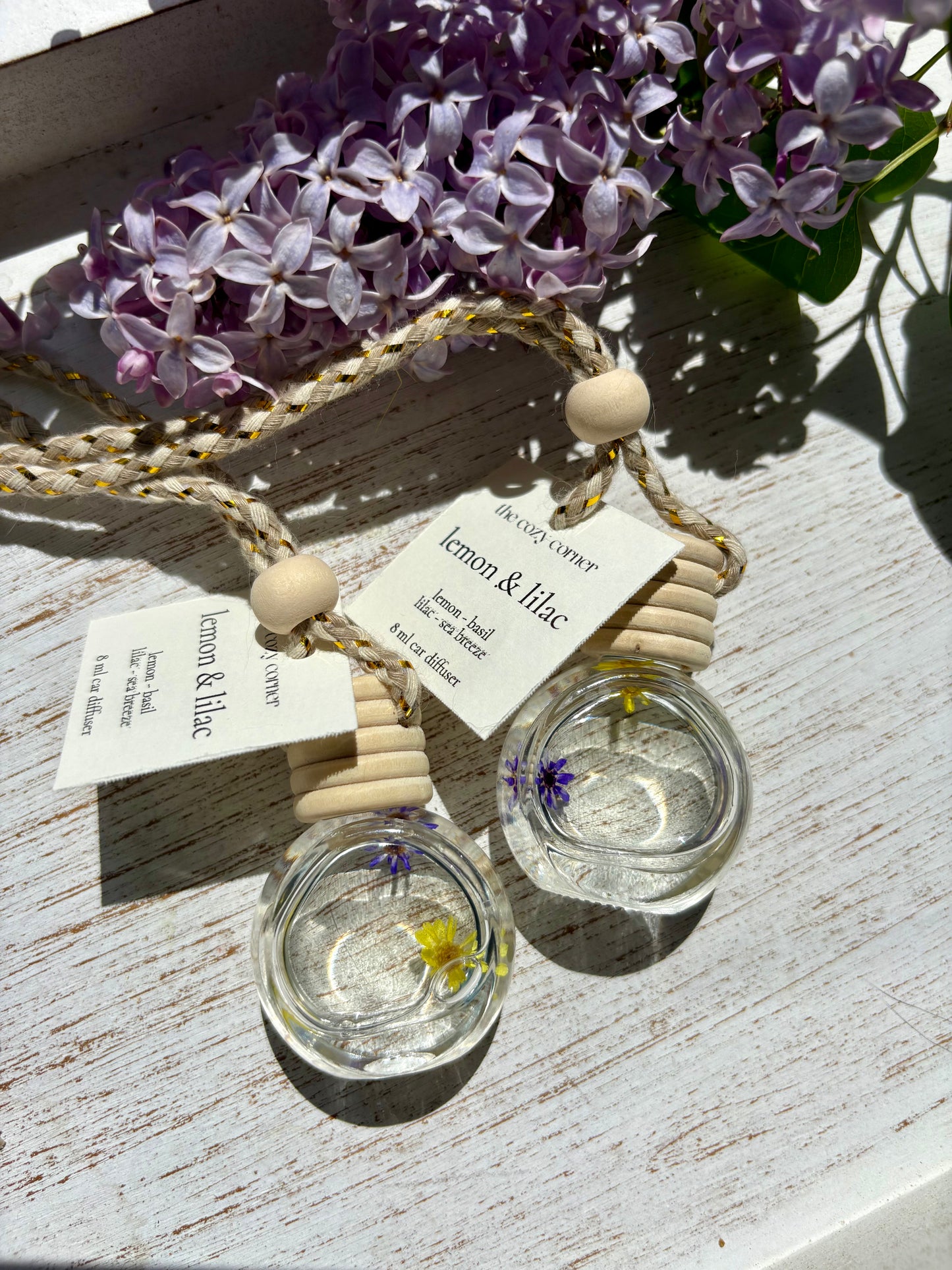 Two small glass containers with floral elements on a wooden surface with purple flowers in the background.