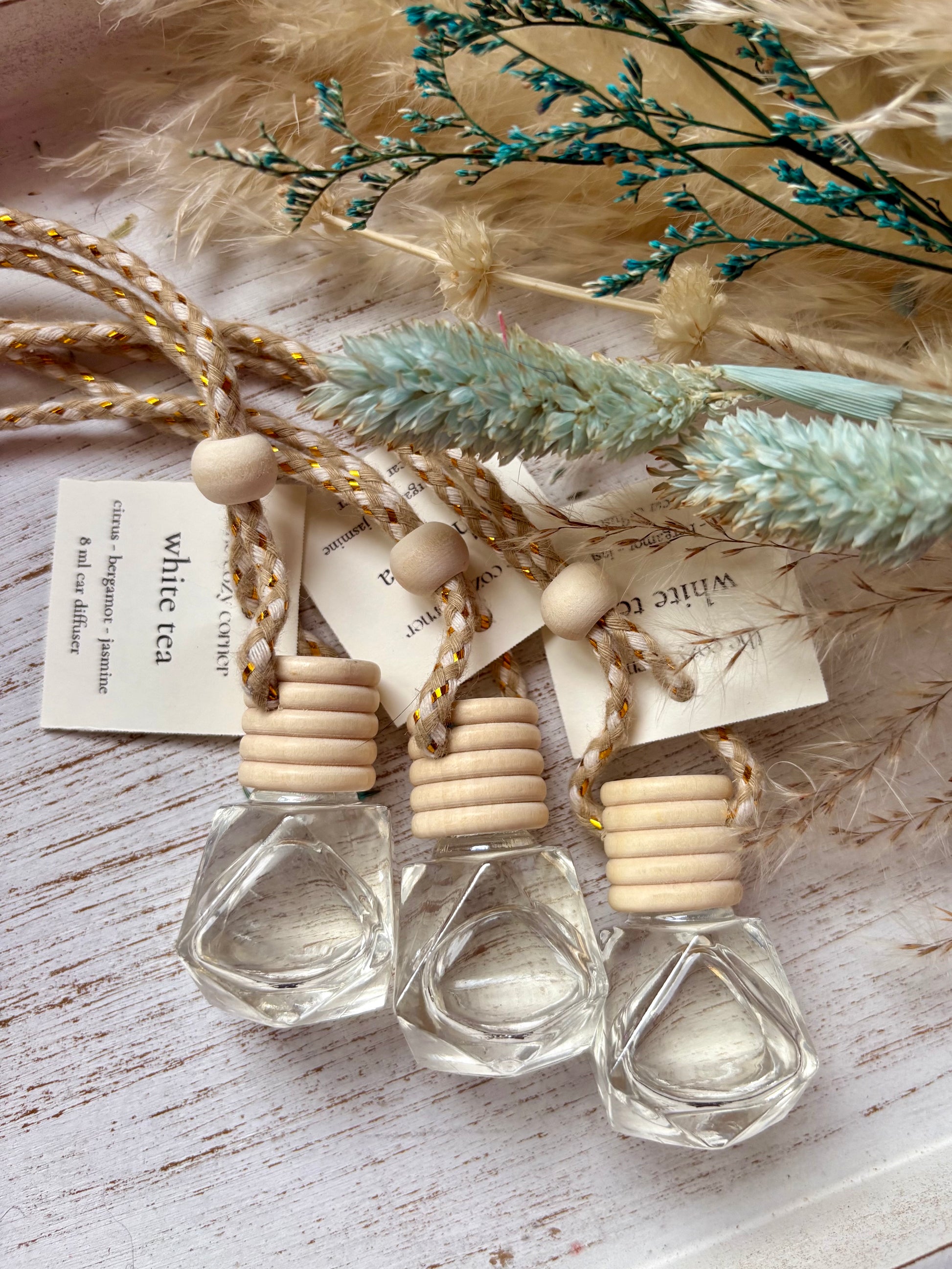 Three small clear bottles with wooden caps on a rustic wooden surface with dried plants.