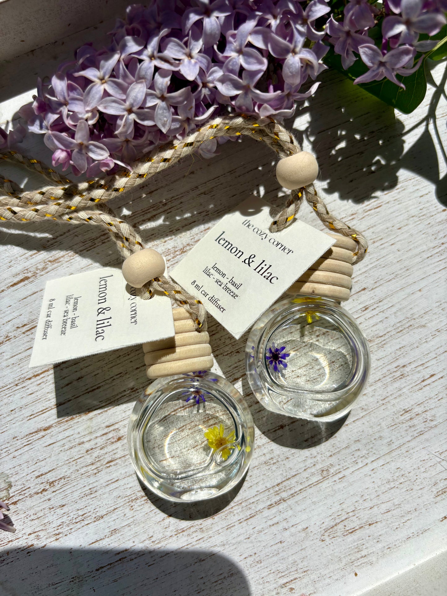 Two small glass containers with floral elements on a wooden surface with purple flowers in the background.
