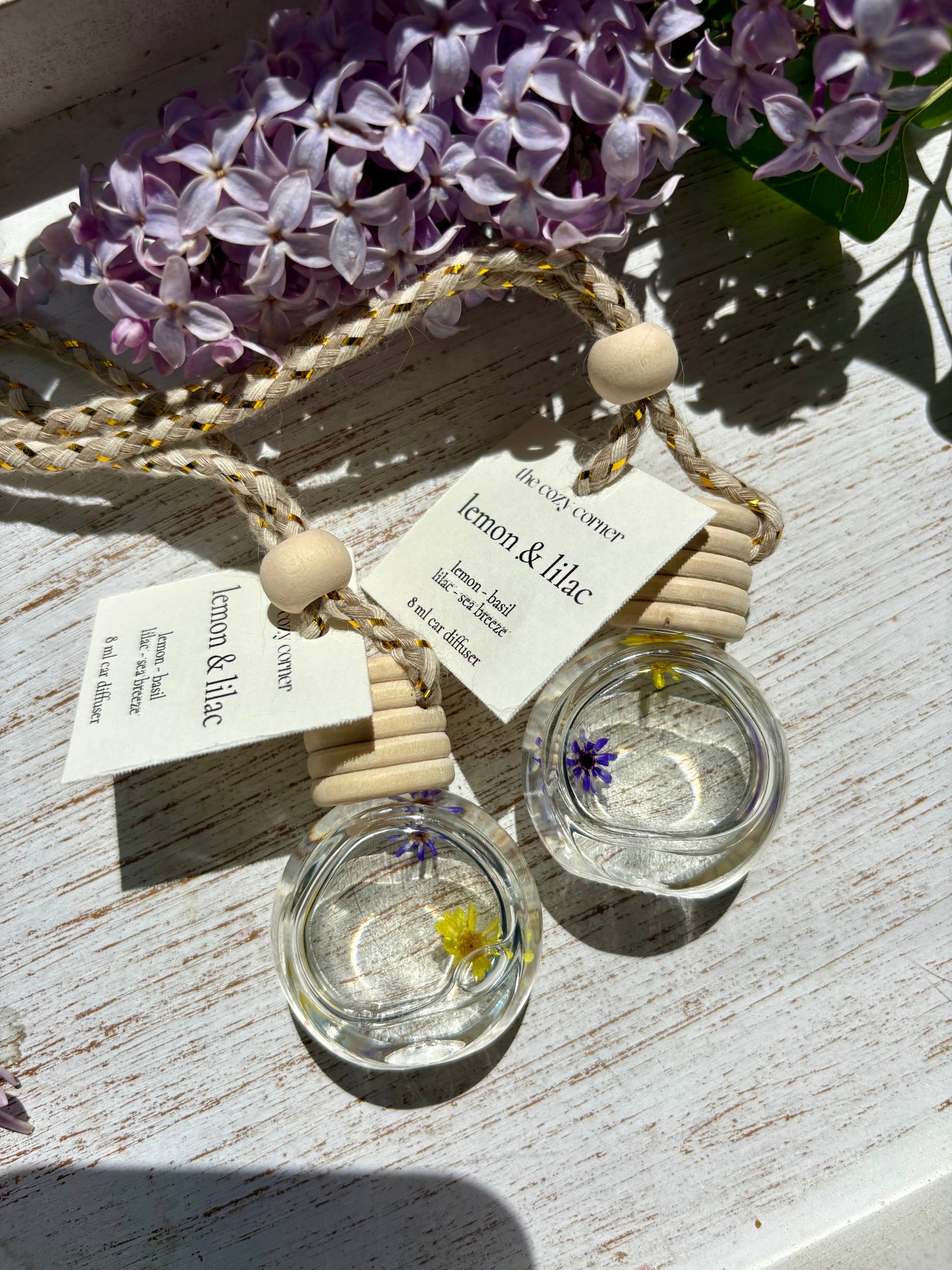 Two small glass containers with floral elements on a wooden surface with purple flowers in the background.