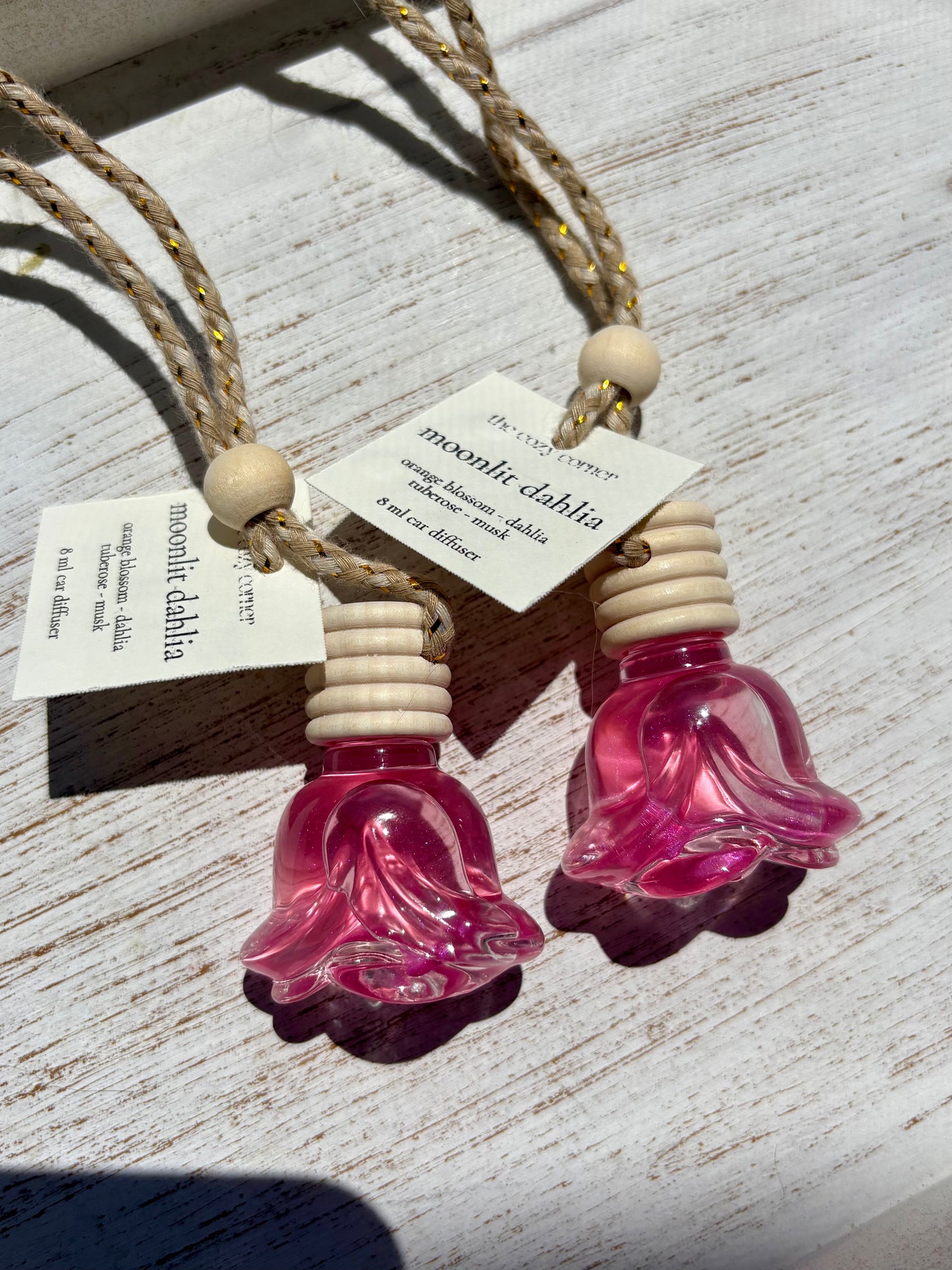 Two pink glass flower-shaped containers with wooden bases on a light wooden surface.